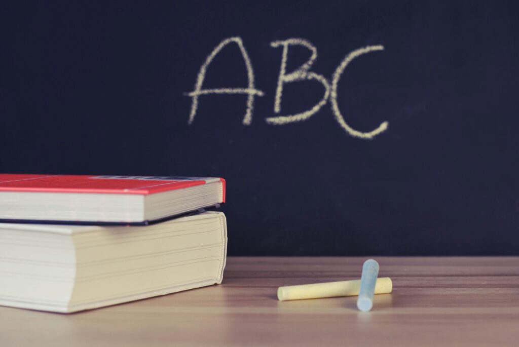 Stack of books and chalk on desk with ABC on blackboard background.